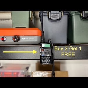 May include: A black two-way radio with an antenna and a lanyard. The radio has a green screen and a keypad. The radio is on a shelf with a sign that says "Buy 2 Get 1 FREE".