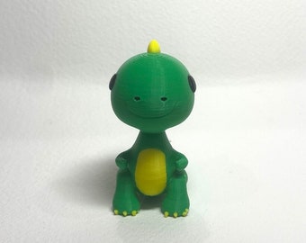 May include: A small green dinosaur toy with a yellow belly and black eyes. The dinosaur is sitting with its legs crossed and has a small yellow horn on its head.