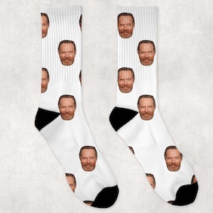 May include: A pair of white socks with a repeated pattern of a man's face. The socks have black heels and toes.