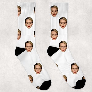 Peut inclure: Une paire de chaussettes blanches avec un motif répété d'un visage de femme. Les chaussettes ont des talons et des orteils noirs.