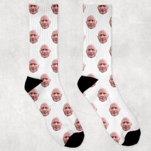 Può includere: Un paio di calzini bianchi con un motivo ripetuto di un viso maschile. I calzini sono realizzati in un materiale morbido e confortevole e sono perfetti per l'uso quotidiano.