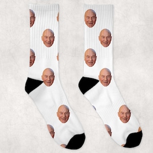 May include: White socks with a repeated pattern of a man's face. The socks are black at the toe and heel.