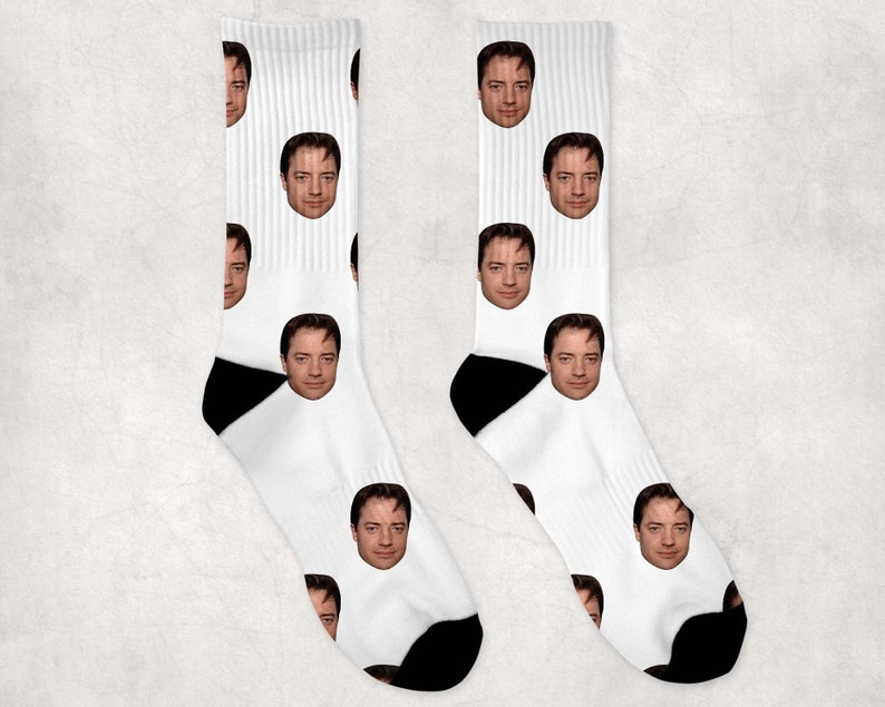 May include: A pair of white socks with a repeated pattern of a man's face. The socks have black heels and toes.