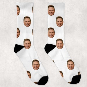 May include: A pair of white socks with a repeated pattern of a man's face. The socks have black heels and toes.