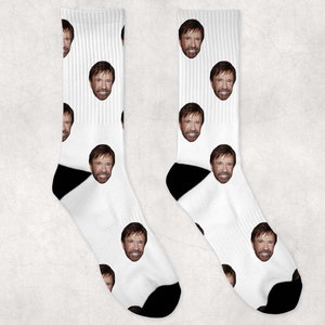May include: A pair of white socks with a repeated pattern of a man's face. The socks have black heels and toes.