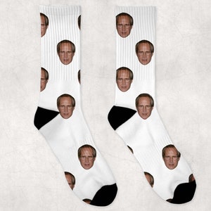 May include: A pair of white socks with a repeated pattern of a man's face. The socks have black heels and toes.