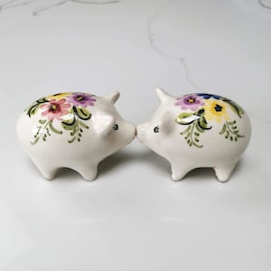 May include: A white ceramic mug with a black handle and the text "But First, Coffee" in a bold, black font. The mug is set against a blurred background, suggesting a cosy setting.