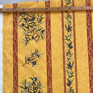 Könnte beinhalten: Gelber Stoff mit einem sich wiederholenden Muster aus Olivenzweigen mit grünen und schwarzen Oliven. Der Stoff hat rote und goldene Streifen mit einem dekorativen Muster.