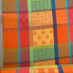 May include: A colorful fabric tablecloth with a checkered pattern and floral designs in shades of orange, red, yellow, green, and blue.