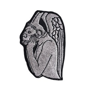 May include: Embroidered patch featuring a gray gargoyle with detailed wings and hands covering its face. The patch has a black border and is likely designed to be ironed or sewn onto fabric. The design is a gothic or architectural theme.