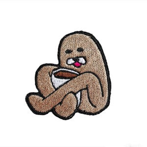 Peut inclure: Écusson brodé représentant un personnage de dessin animé brun, tenant une tasse de café. Le personnage a une expression surprise, une langue rose et une moustache blanche. L'écusson est bordé de noir.