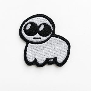 Peut inclure: Patch brodé blanc représentant une créature de dessin animé avec de grands yeux noirs et une bouche simple. La créature a une tête ronde et un petit corps.