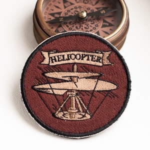 May include: A maroon embroidered patch with a helicopter design. The helicopter is beige and has a banner that reads "HELICOPTER".