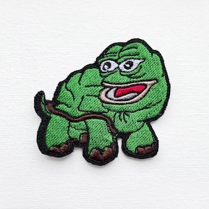 Puede incluir: Parche bordado verde de una rana de dibujos animados con una amplia sonrisa, que lleva una concha y está sentada sobre sus patas traseras.