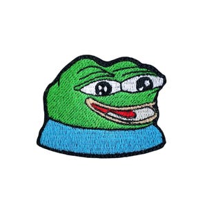 Può includere: Toppa ricamata raffigurante una rana verde sorridente, con occhi bianchi e colletto blu. La toppa, in stile cartoon, è progettata per essere applicata su abbigliamento o accessori.
