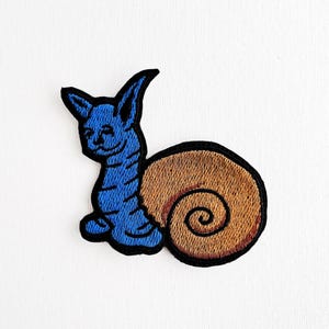 Peut inclure: Patch brodé bleu et marron d'un escargot avec un visage souriant.