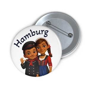 Könnte beinhalten: Ein weißer Button mit einer Cartoon-Illustration von zwei Kindern, einem Jungen in Matrosenanzug und einem Mädchen in Tracht, mit dem Wort "Hamburg" in Marineblau. Ein zweiter Button ist sichtbar.