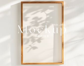 May include: A wooden frame with a white background. The frame is sitting on a white surface with shadows from a window. The text "Mockup" and "Papier" is visible in the frame.