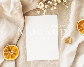Puede incluir: Una maqueta de tarjeta blanca con el texto "Mockup Papier PSD.JPG" sobre un fondo beige con rodajas de naranja secas y flores blancas.