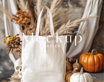 Puede incluir: Una bolsa de lona blanca con un fondo de arpillera marrón. La bolsa está sentada junto a una calabaza blanca y algunas calabazas naranjas.