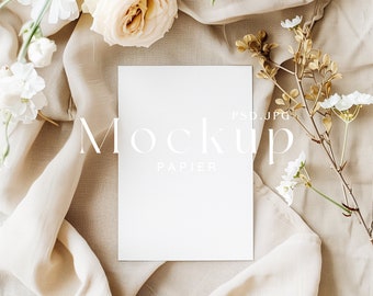 Puede incluir: Una maqueta de tarjeta blanca con el texto "Mockup Papier" sobre un fondo de tela beige con flores blancas y marrones.