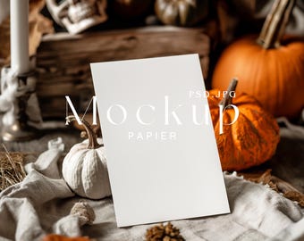 Op de afbeelding: Een witte blanco kaart mockup met de tekst "Mockup Papier PSD, JPG" op een rustiek houten oppervlak met pompoenen en herfstdecoratie.