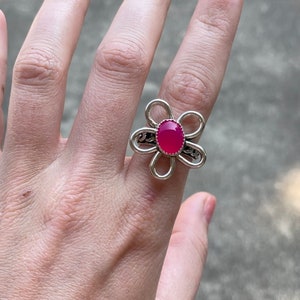 May include: A silver flower ring with a pink oval gemstone in the center.