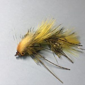 May include: A yellow and brown fly fishing lure with a long tail and a small orange head.