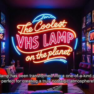 May include: A neon sign that reads "The Coolest VHS LAMP on the planet" in a retro style. The sign is mounted on a black wall with other neon signs and vintage movie posters.