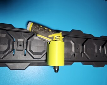 Può includere: Un trapano avvitatore a batteria giallo e nero con manico nero e canna gialla è montato su un rack di stoccaggio a parete nero.