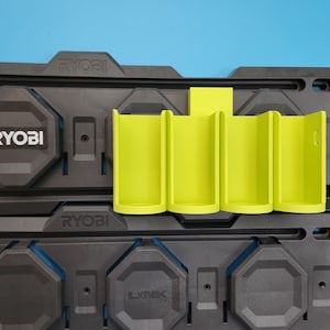 May include: A black and green wall-mounted storage system with the Ryobi logo. The system has a green holder for multiple batteries.