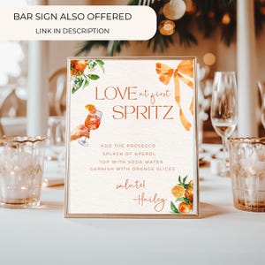 Puede incluir: Un letrero rectangular con marco dorado que dice "LOVE at first SPRITZ". Incluye ilustraciones de acuarela de naranjas y un c&oacute;ctel. Tambi&eacute;n se ve el texto "ADD THE PROSECCO" y "GARNISH WITH ORANGE SLICES".