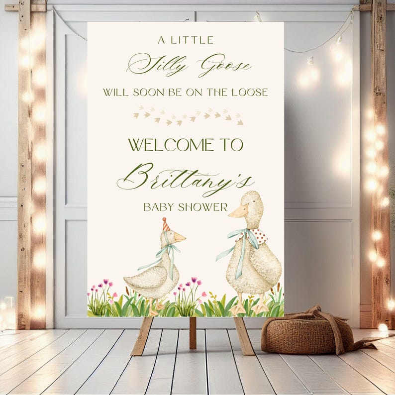 May include: A white welcome sign with green text that reads "A little Silly Goose will soon be on the loose. Welcome to Brittany's Baby Shower". The sign features two cartoon geese, one wearing a party hat, standing in a field of green grass and pink flowers.