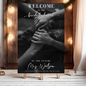 Pu&ograve; includere: Un cartello di benvenuto in bianco e nero per un bridal shower con il testo "Benvenuti al bridal shower della futura Signora Watson 10.25.20XX 90 giorni prima del grande giorno!" Il cartello presenta una foto ravvicinata di due mani intrecciate.