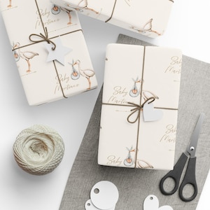May include: Three white gift boxes with brown twine and white tags. The boxes are decorated with a watercolor illustration of a stork carrying a baby in a basket. The text "Baby Martinez" is written on each box.