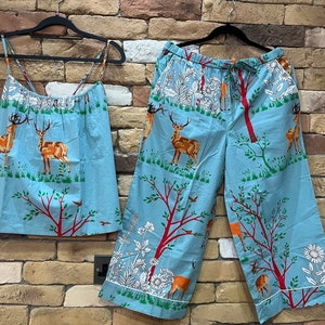 May include: A blue pajama set with a forest print featuring deer, trees, and flowers. The top is a tank top with thin straps and the bottom is a pair of wide-leg pants.