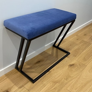 Op de afbeelding: Een blauwe gestoffeerde bank met een zwart metalen frame. De bank heeft een eenvoudig, modern ontwerp en is perfect voor een hal of entree.