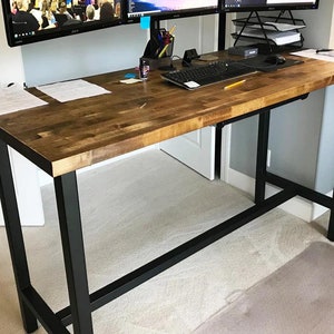 May include: A standing desk with a wood top and black metal legs. The desk has a keyboard tray and is set up with two computer monitors.