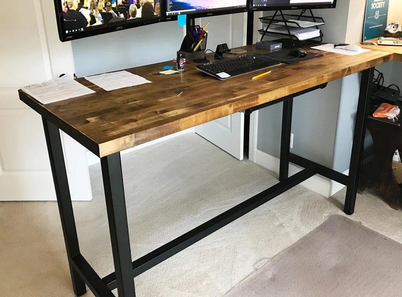 May include: A standing desk with a wood top and black metal legs. The desk has a keyboard tray and is set up with two computer monitors.