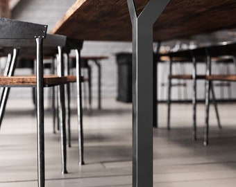 May include: A close-up of a black metal table leg with a Y-shaped support. The leg is attached to a wooden table top.