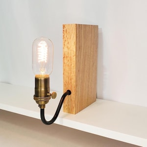May include: A wooden block lamp with a vintage-style light bulb. The lamp features a brass bulb holder and a black, curved cord. The wooden block has a natural wood grain finish, and the bulb is a clear glass tube.