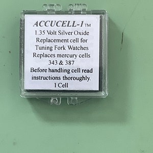 May include: A clear plastic container with a white label that reads "ACCUCELL-1 TM 1.35 Volt Silver Oxide Replacement cell for Tuning Fork Watches Replaces mercury cells 343 & 387 Before handling cell read instructions thoroughly. 1 Cell"