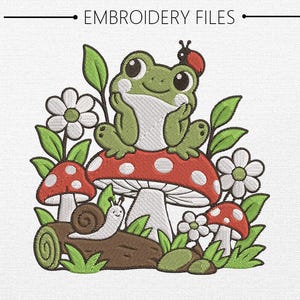 Può includere: Un disegno per ricamo raffigurante una rana verde con una coccinella sulla testa, seduta su un grande fungo rosso a pois bianchi. La scena include un tronco marrone con una lumaca, foglie verdi e fiori bianchi. Il testo EMBROIDERY FILES è in alto.