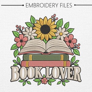 May include: An embroidery design featuring a stack of two books topped with an open book, surrounded by a sunflower, white daisies, pink flowers, and green leaves. The text "BOOK LOVER" is embroidered in large, light-colored block letters below.