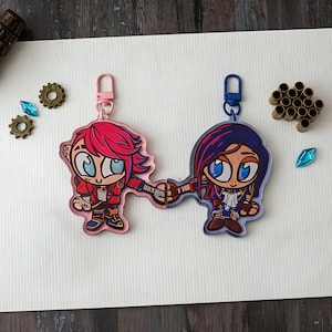 Peut inclure: Deux porte-clés représentant des personnages de dessins animés. L'un présente un personnage aux cheveux roses et une veste rouge, l'autre a des cheveux bleus et une veste bleue. Les deux se tiennent la main. Chaque porte-clés a un fermoir.