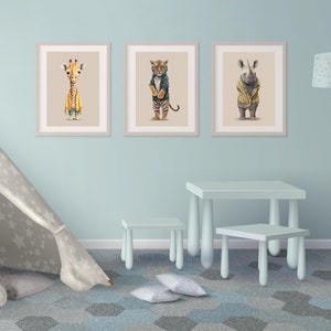 Puede incluir: Tres ilustraciones enmarcadas de animales con ropa. Las ilustraciones son de una jirafa, un tigre y un rinoceronte. Los marcos son blancos y las ilustraciones están en una pared azul claro.
