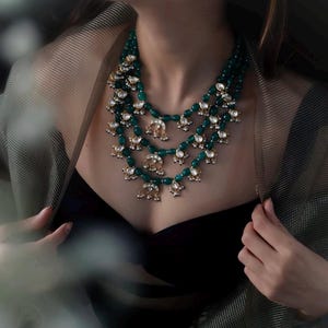 Op de afbeelding: Een gelaagde smaragdgroene en gouden ketting met traanvormige kralen en decoratieve accenten.