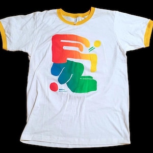 May include: A white ringer t-shirt with yellow trim on the collar and sleeve cuffs. The front features a large, abstract graphic design composed of a red-to-orange gradient shape, a blue-to-green gradient shape, a small yellow circle, and a red circle.