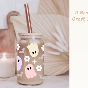 May include: A glass jar with a wooden lid and a straw, decorated with a pattern of ghosts, bats, and flowers. The jar is filled with a brown liquid. "A Great Craft Idea" is written in the upper right corner of the image.