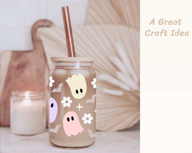 May include: A glass jar with a wooden lid and a straw, decorated with a pattern of ghosts, bats, and flowers. The jar is filled with a brown liquid. "A Great Craft Idea" is written in the upper right corner of the image.